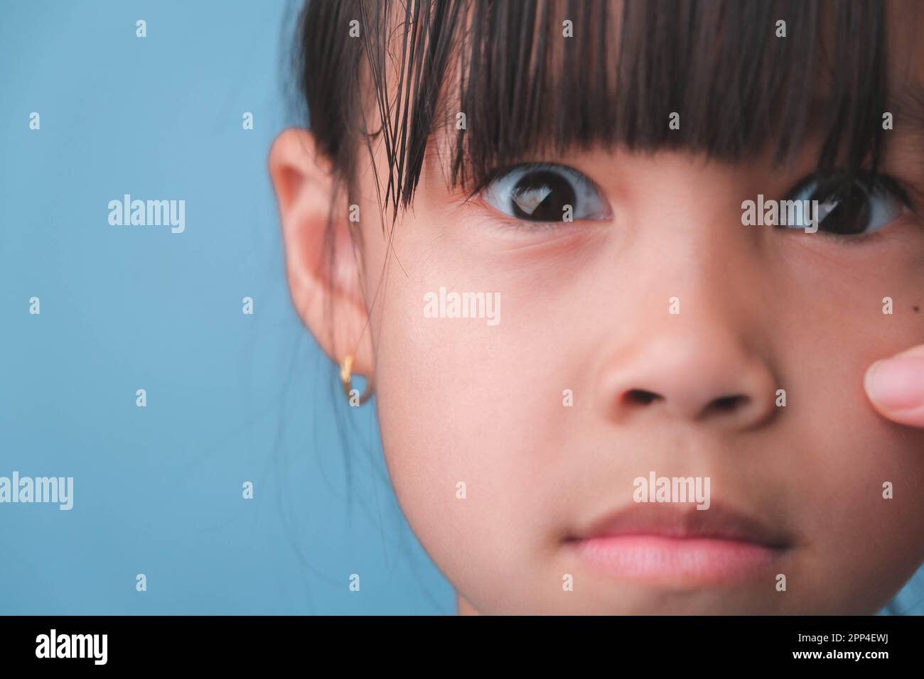 Close-up portrait of surprised young Asian girl isolated on blue background. Cute shocked young girl with big black eyes reacts surprisingly to someth Stock Photo