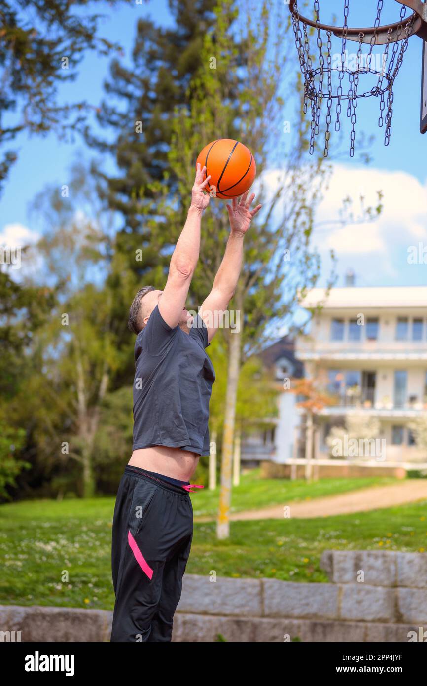 Middle age man in black sports shorts jumping and throwing baskets while playing basketball on a sports field Stock Photo