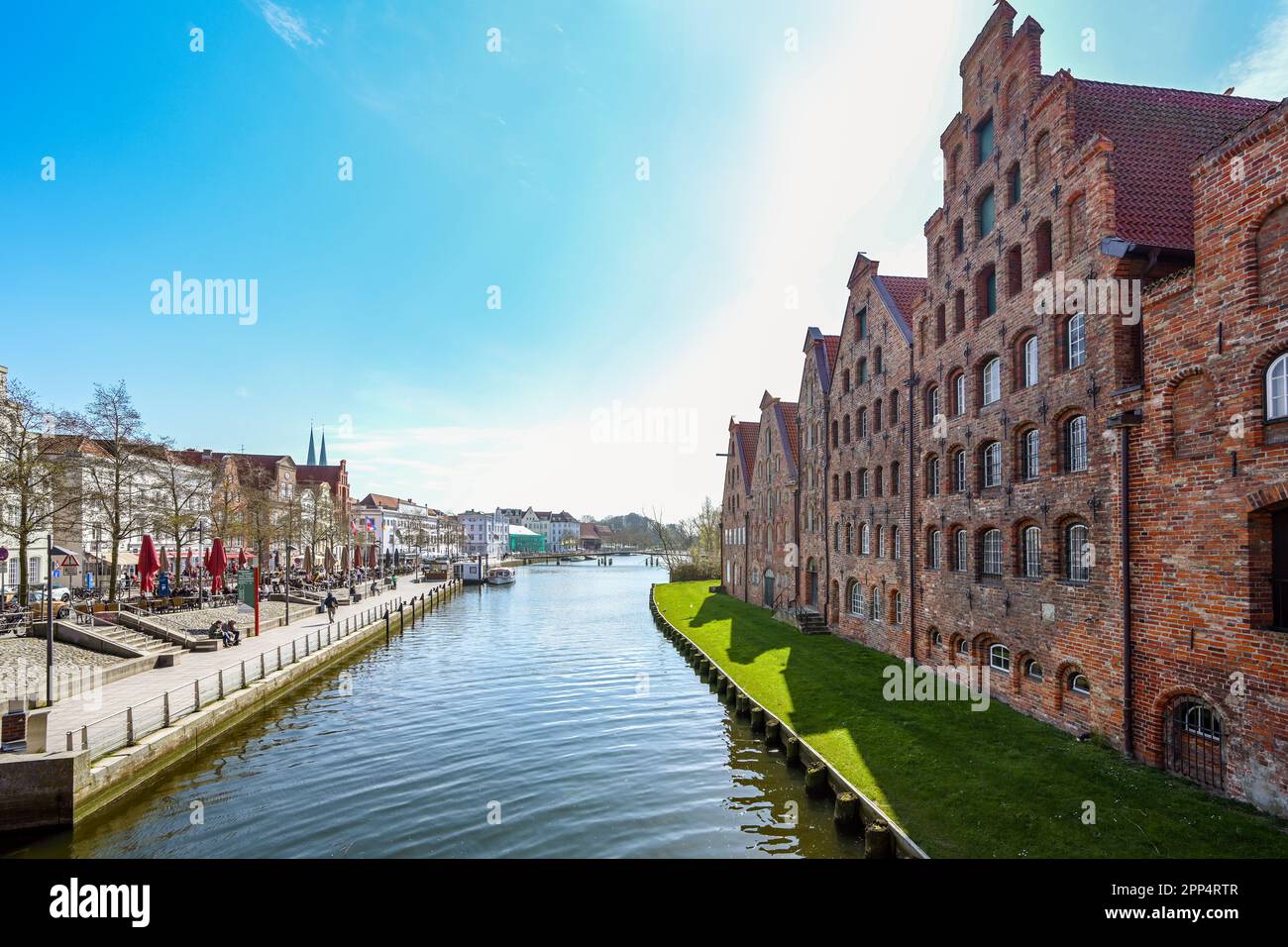 Lubeck, Germany, April 17, 2023: Historic salt store buildings and promenade with cafes on the banks of the river Trave in the old town of Luebeck, to Stock Photo