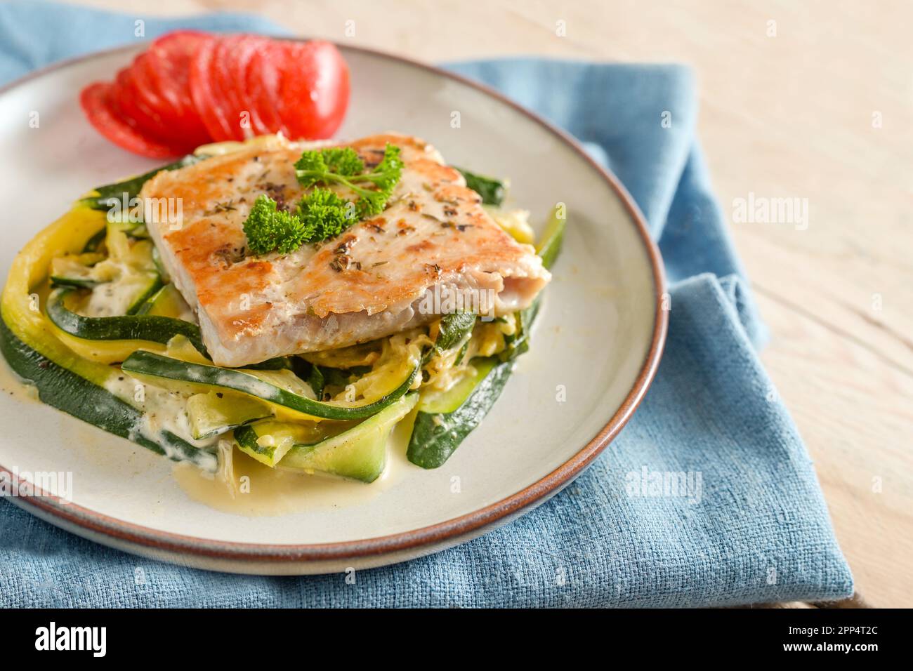 Salmon fillet with parsley garnish, zucchini vegetables and tomato on a