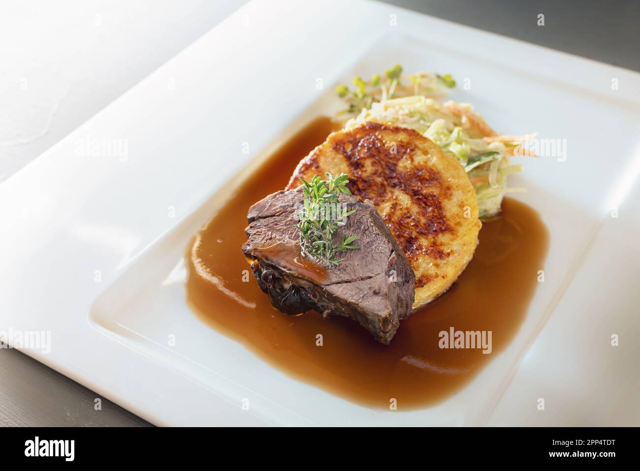 Roast deer, flat bread dumpling and round shaped cabbage vegetable with brown sauce and thyme garnish on a white plate, main course in a menu, copy sp Stock Photo