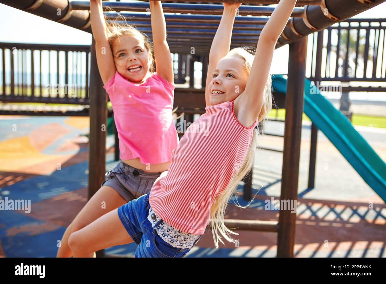 Sisters make the best of friends. two little girls hanging on the monkey bars at the playground. Stock Photo