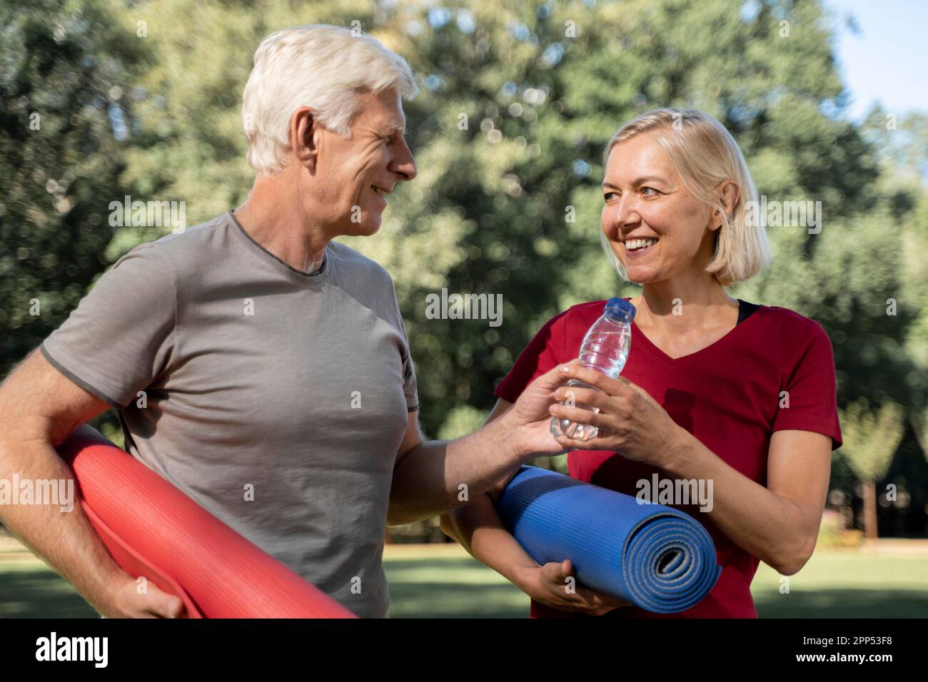 Smiley older couple outdoors with yoga mats water bottle Stock Photo