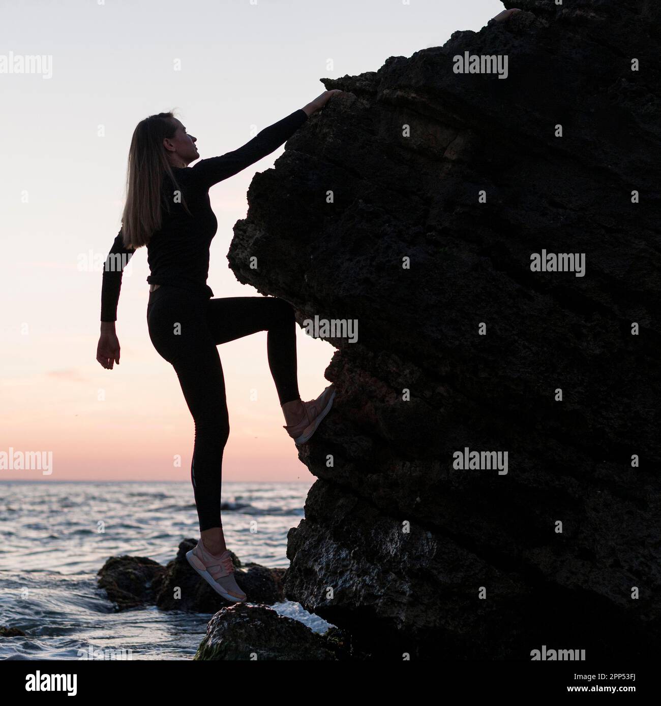 Sideways woman climbing rock ocean Stock Photo