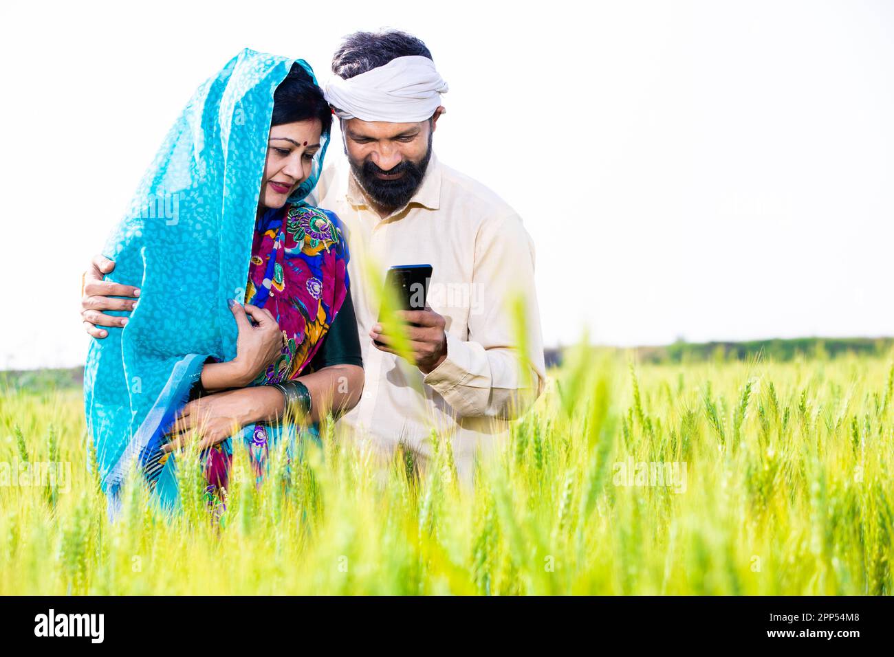 Happy young indian farmer couple using smart phone at wheat agriculture ...