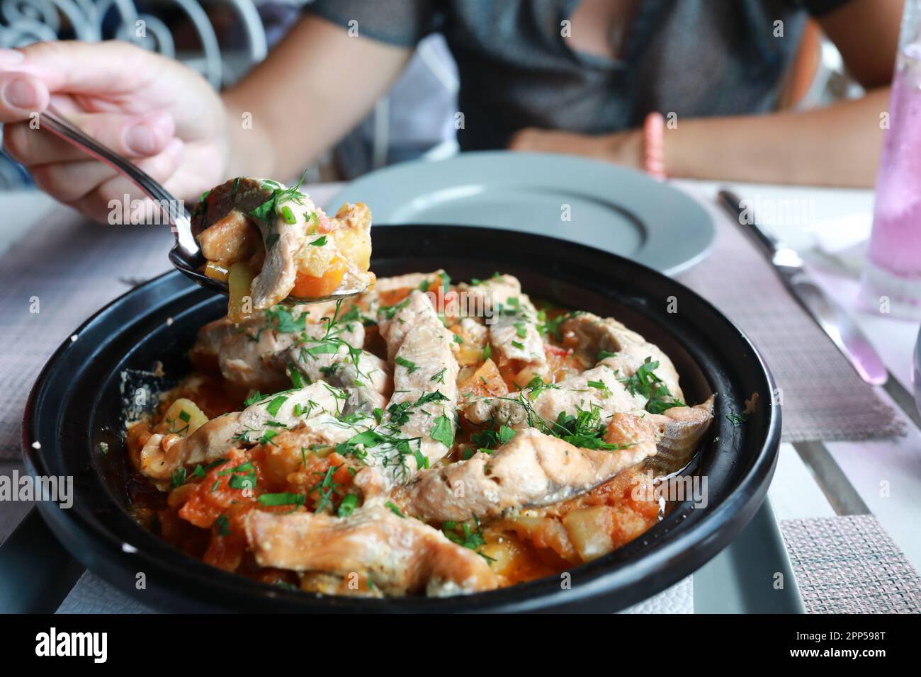 Person eating fish with vegetables in tagine in restaurant Stock Photo