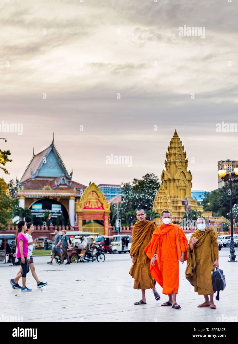 Phnom Penh,Cambodia-January 4th 2023:Khmer monks,wearing facemasks,walk along the pedestrianizsed Sisowath Quay,in front of the Royal Palace, at sunse Stock Photo