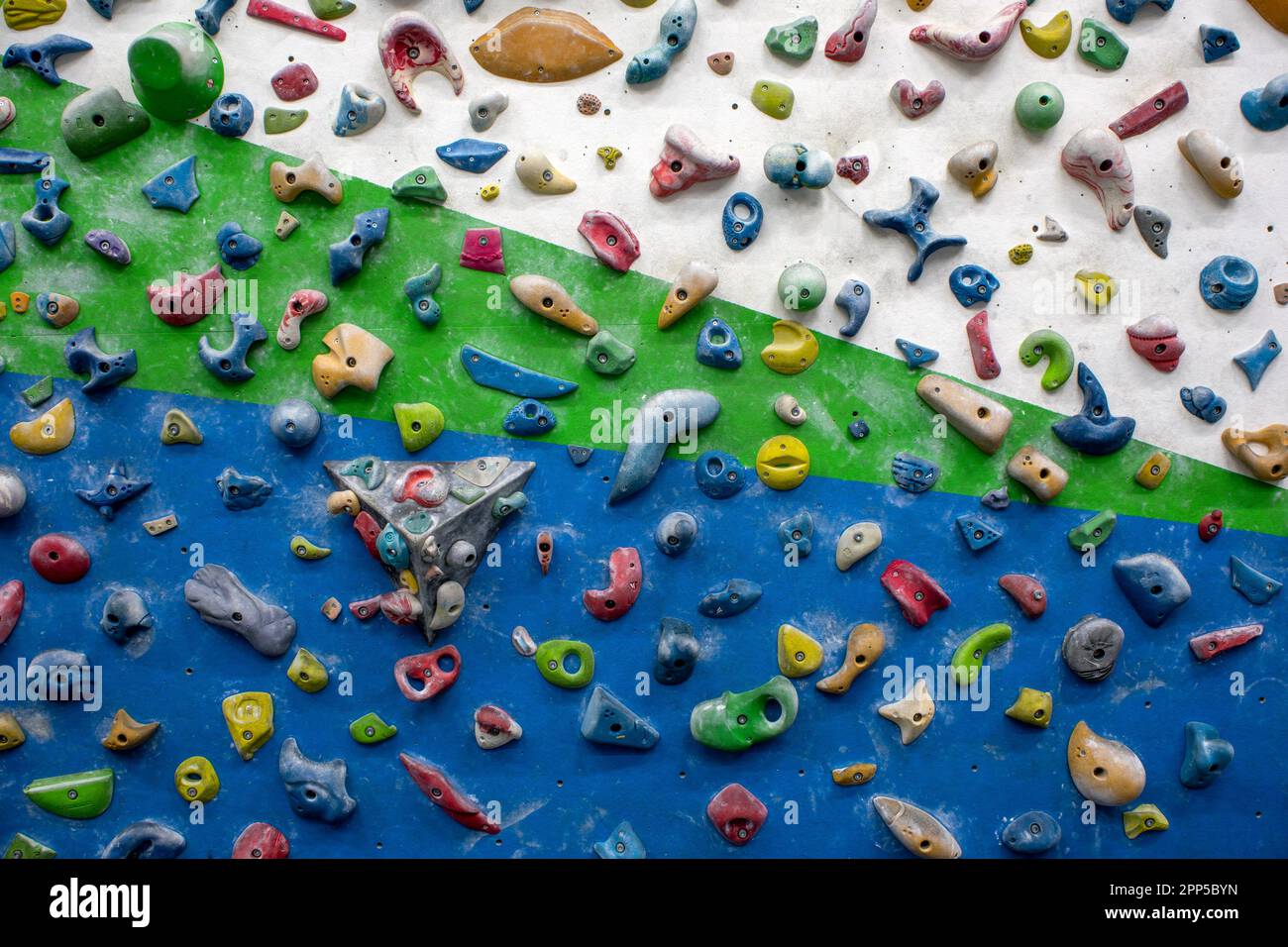 Detail of a vertical wall of an indoor climbing wall with holds of different colors to practice climbing Stock Photo