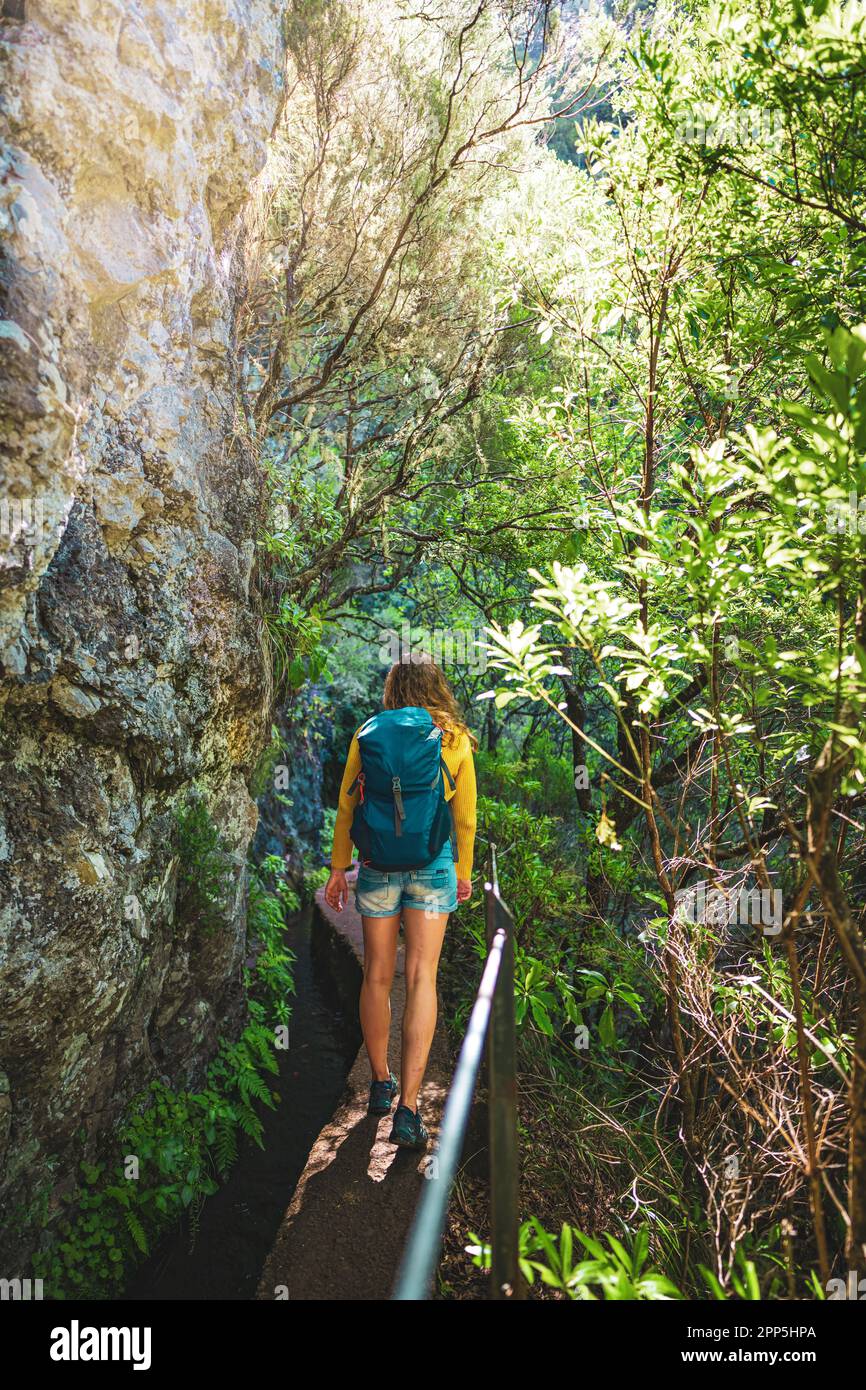 Description: Tourist woman walking along overgrown jungle hiking trail  next to canal through Madeiran rainforest. Levada of Caldeirão Verde, Madeira Stock Photo