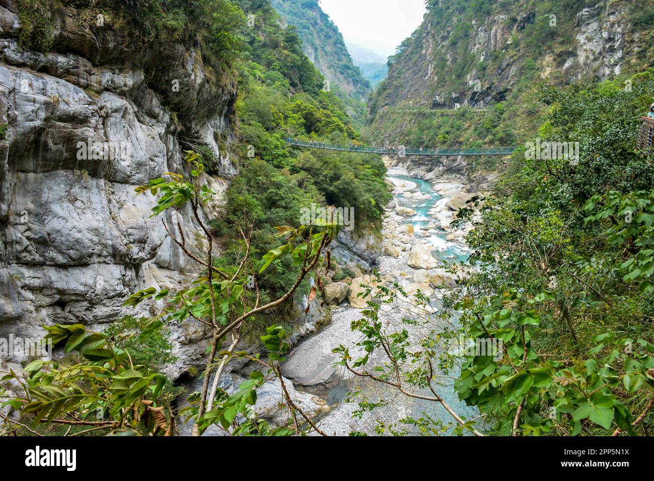 Tourists crossing bridge over narrow turquoise Liwu River Gorge surrounded by green mountain valley of Taroko Gorge in Taroko National Park, Taiwan Stock Photo
