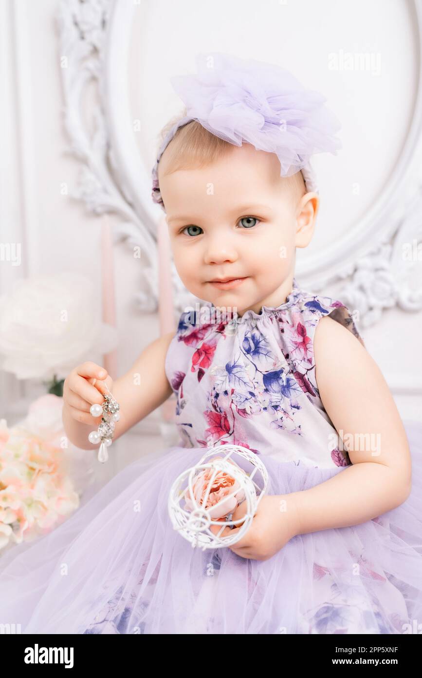 baby girl elegant dress a one year old girl in a puffy dress and a cute bow poses against the backdrop of a bright room with a dressing table and 2PP5XNF