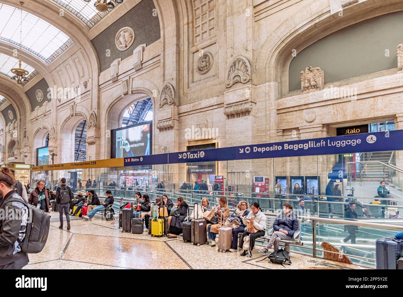 Rail passengers sit waiting with luggage inside the grand interior of