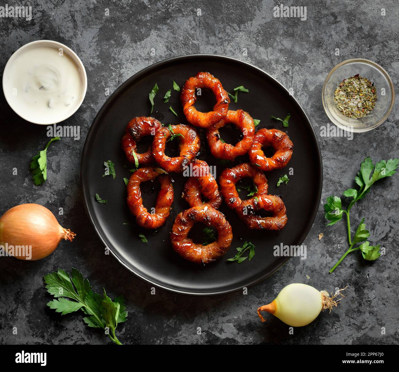 Bacon wrapped onion rings on black plate over dark stone background
