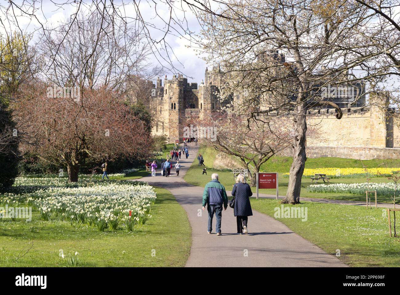 Alnwick Castle Northumberland; A large medieval 12th century castle. Visitors in the castle gardens on a sunny spring day; Alnwick Northumberland UK Stock Photo