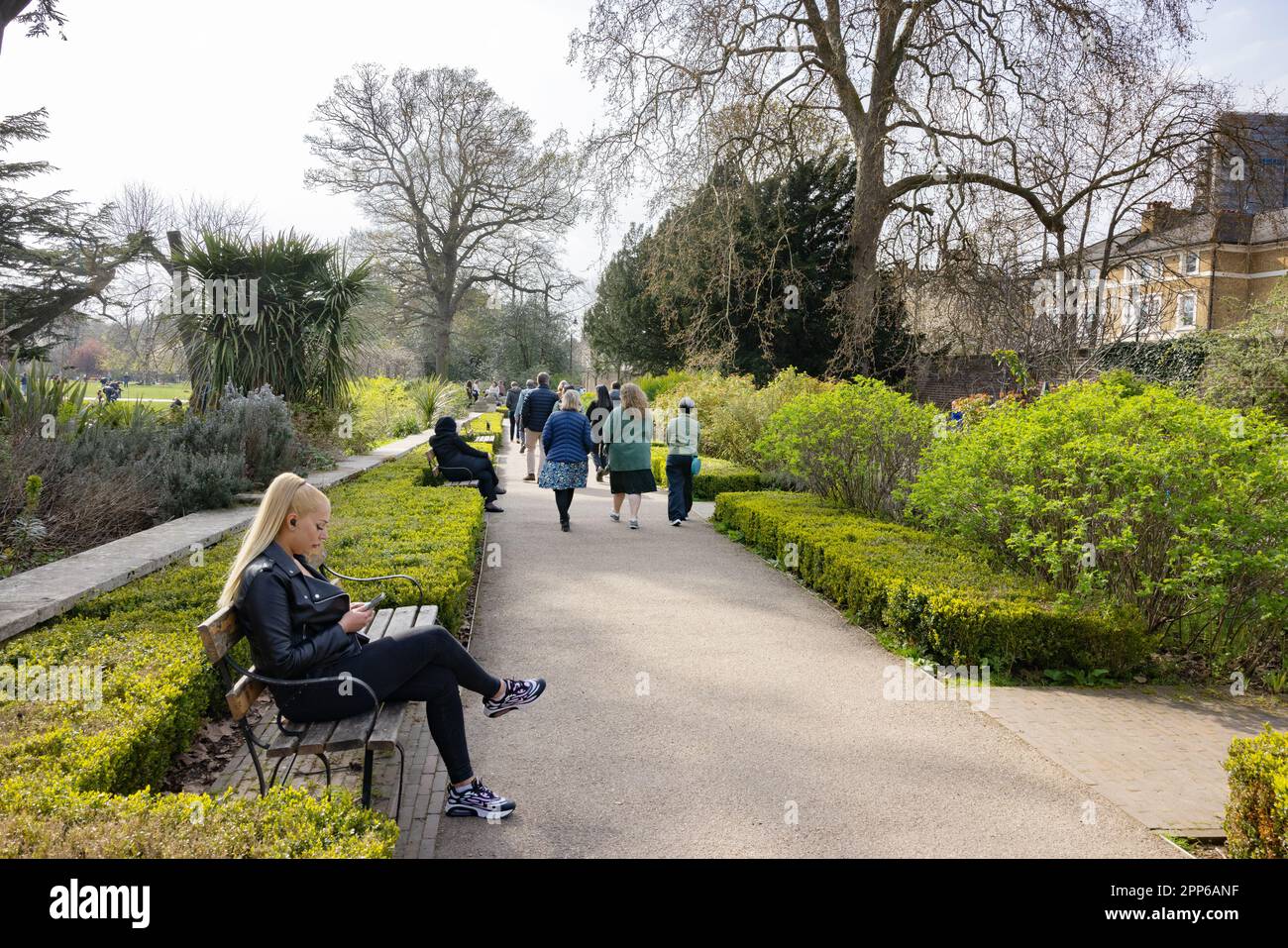 Woman sitting on a bench in a park in spring sunshine; Walpole Park, Ealing, London UK Stock Photo