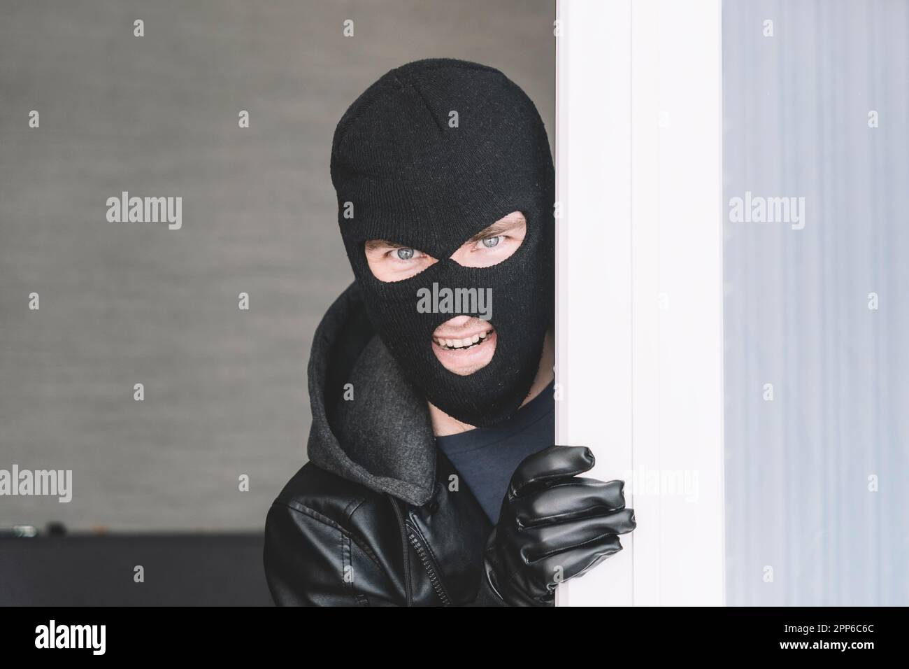 Stealthy criminal wearing black balaclava sneaking into house through window or glass door. copy
