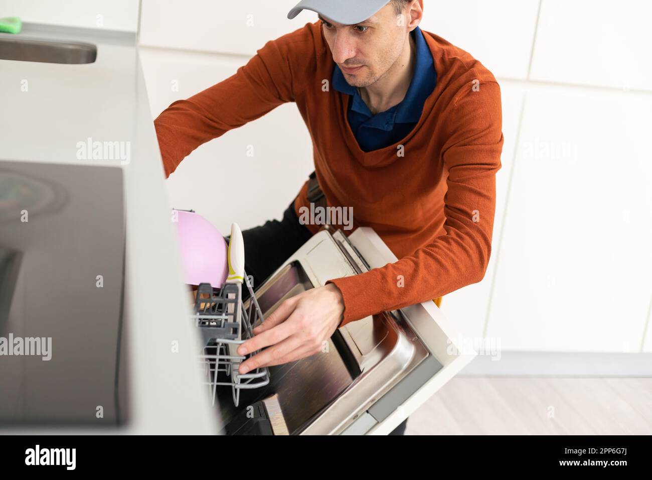 A man or a service worker in special clothes using a screwdriver attaches to the countertop or removes the dishwasher. Stock Photo