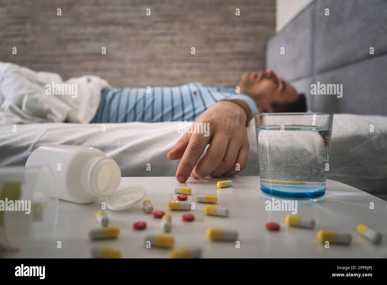 man sleeps on a bed . table with pills and a glass of water. Sleeping pills for a good sleep. Man sleeping - pills on bed table. drug overdose. a leth Stock Photo