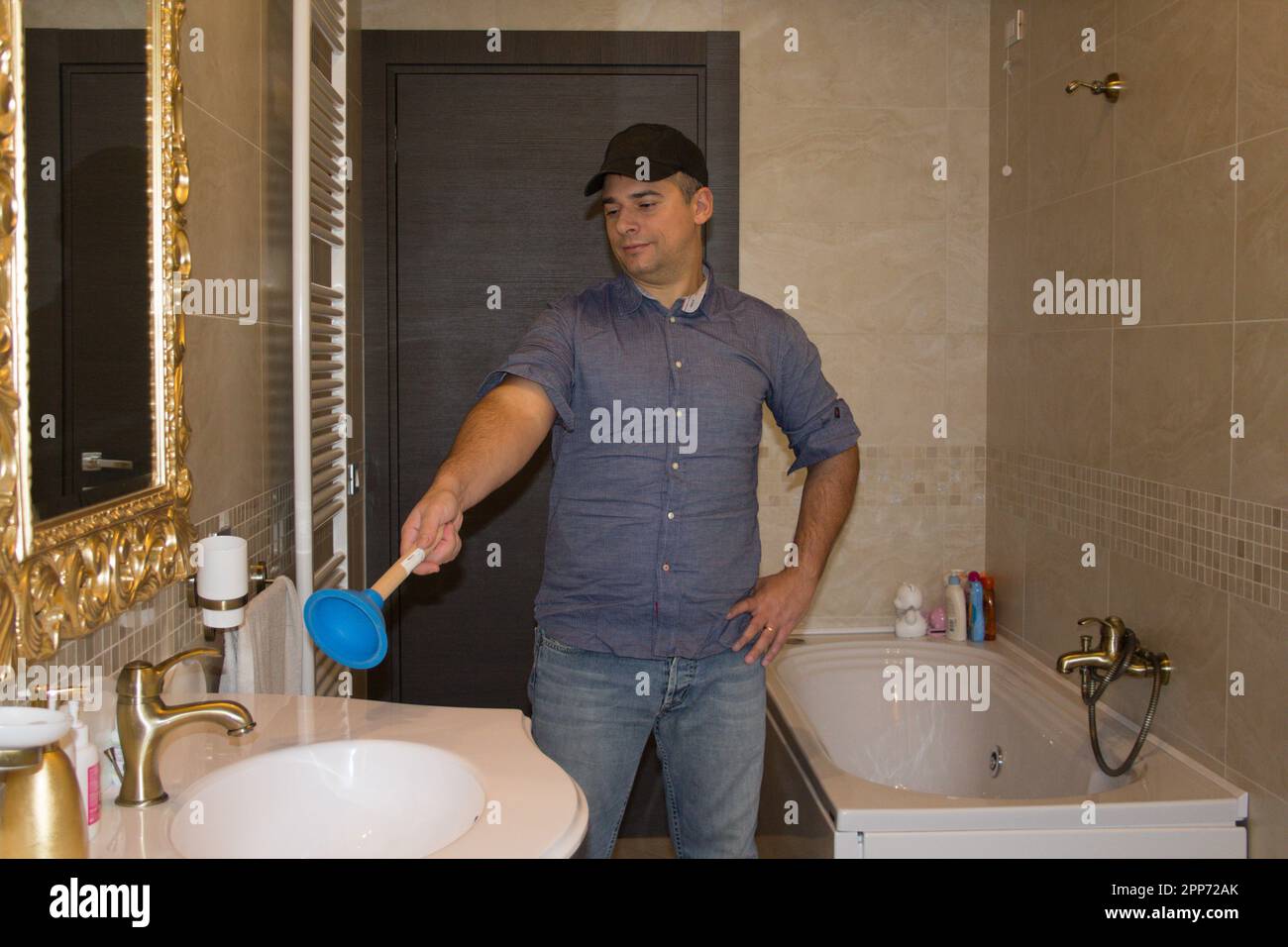 https://c8.alamy.com/comp/2PP72AK/image-of-a-plumber-in-a-bathroom-pointing-with-a-plunger-at-a-clogged-sink-that-needs-repairing-diy-work-at-home-2PP72AK.jpg