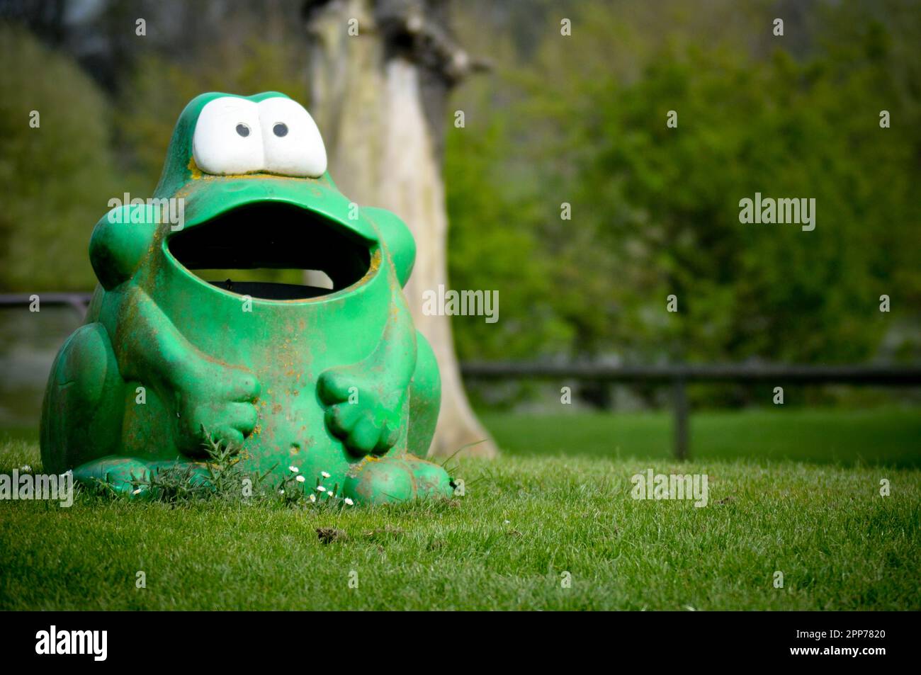 A well weathered, comical green frog shaped plastic rubbish bin in a play park, England Stock Photo