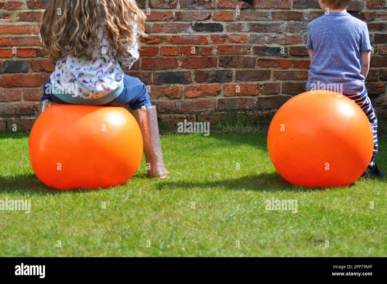 Children bouncing in a garden on an orange space hopper toy Stock Photo