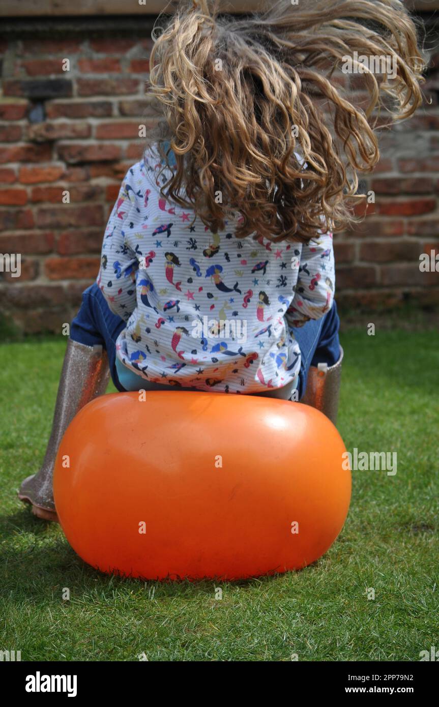 Children bouncing in a garden on an orange space hopper toy Stock Photo