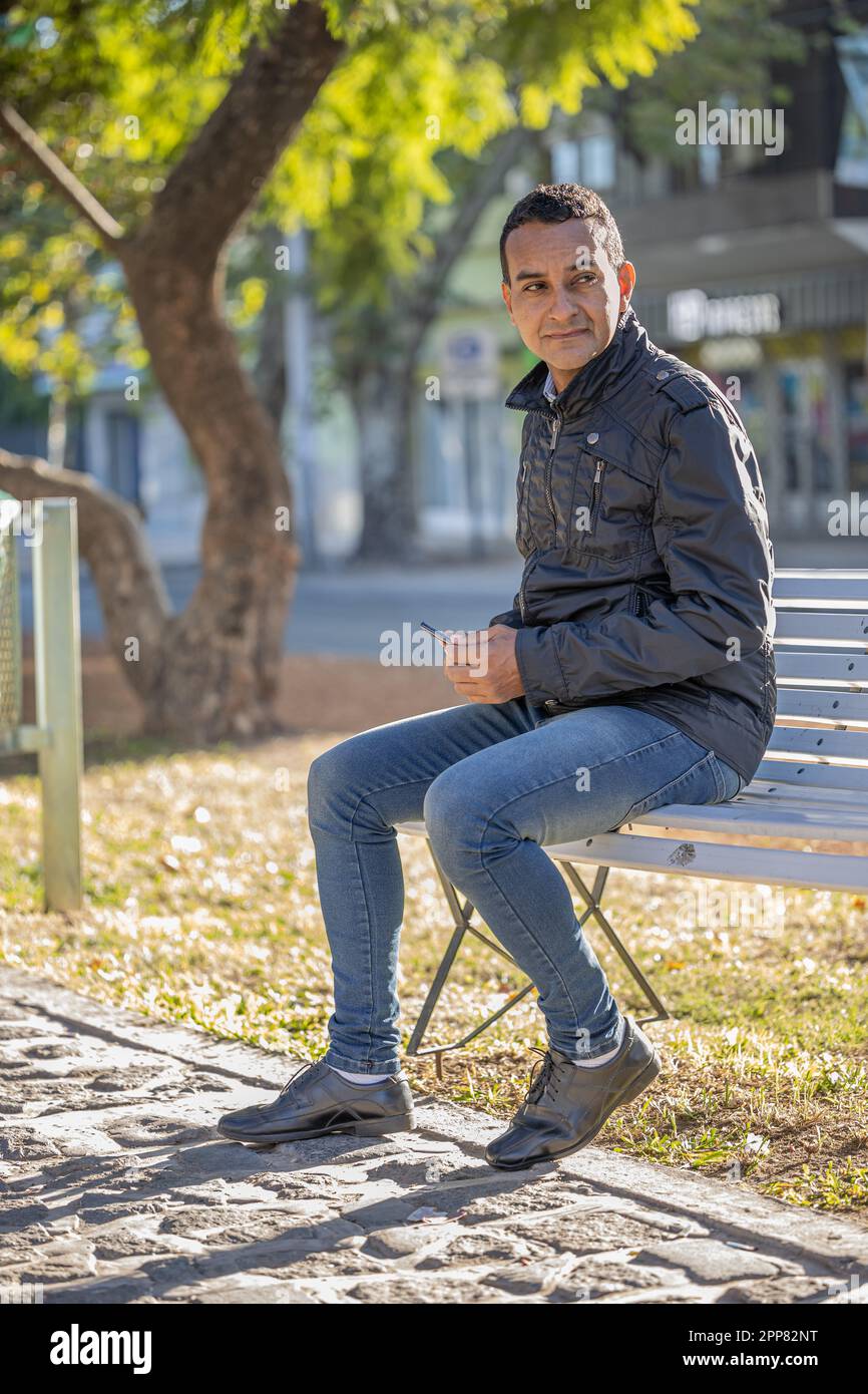 Young latin man sitting on a square bench. Stock Photo