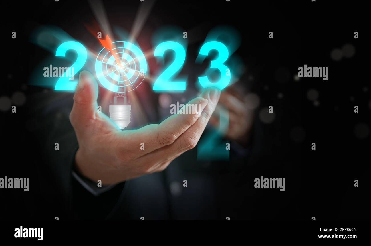 Businessman's hand holding the year 2023 with light blub, dart, and target. Starting new year, business, project, path, goal, or life. Control, manage Stock Photo