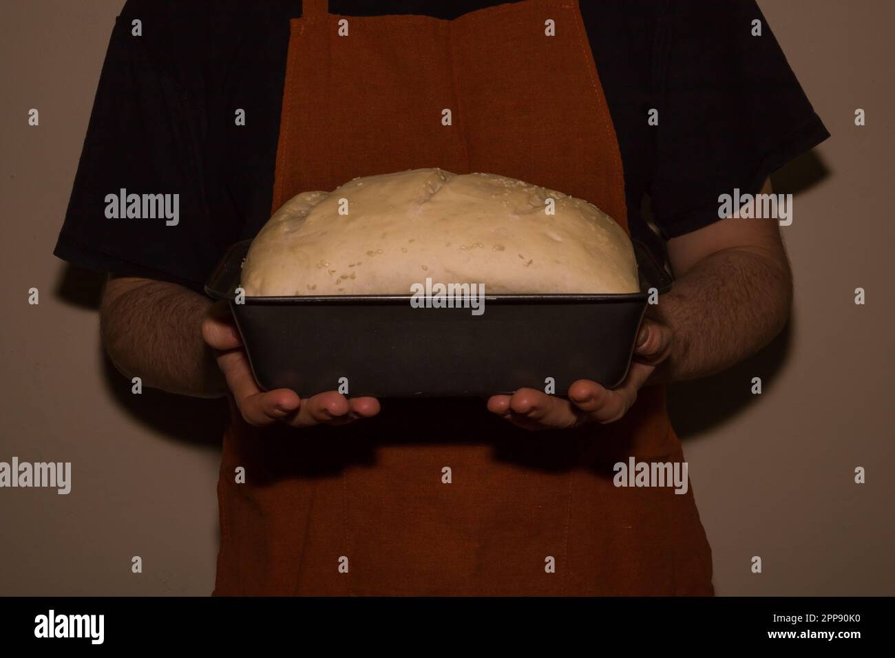 Baker in apron holding a homemade rised bread dough. An old-style home bakery. World cuisine - bread and bakery products Stock Photo