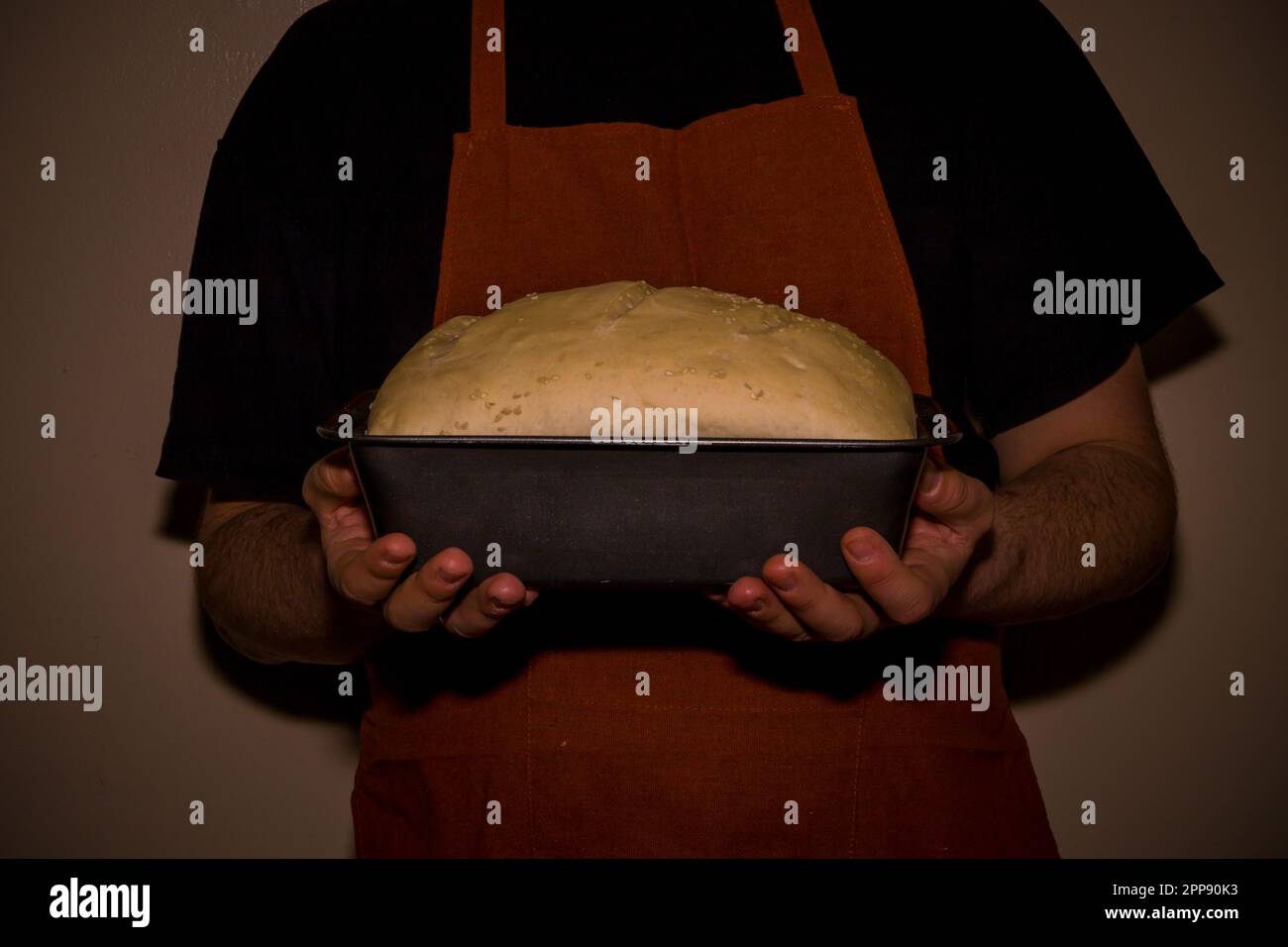 Baker in apron holding a homemade rised bread dough. An old-style home bakery. World cuisine - bread and bakery products Stock Photo