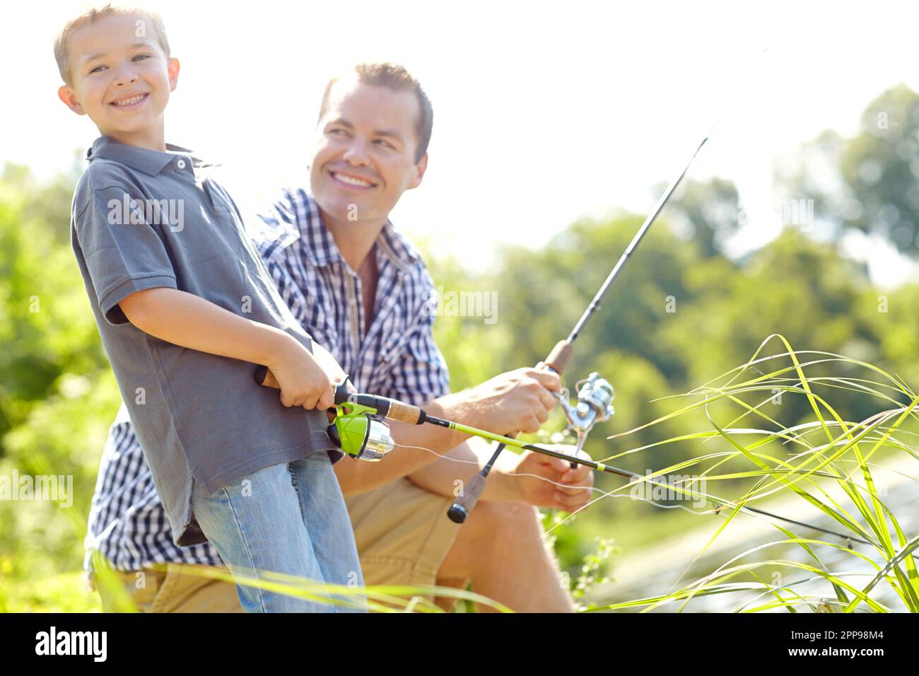https://c8.alamy.com/comp/2PP98M4/just-like-dad-young-father-smiling-with-his-son-while-holding-their-fishing-rods-beside-a-lake-2PP98M4.jpg