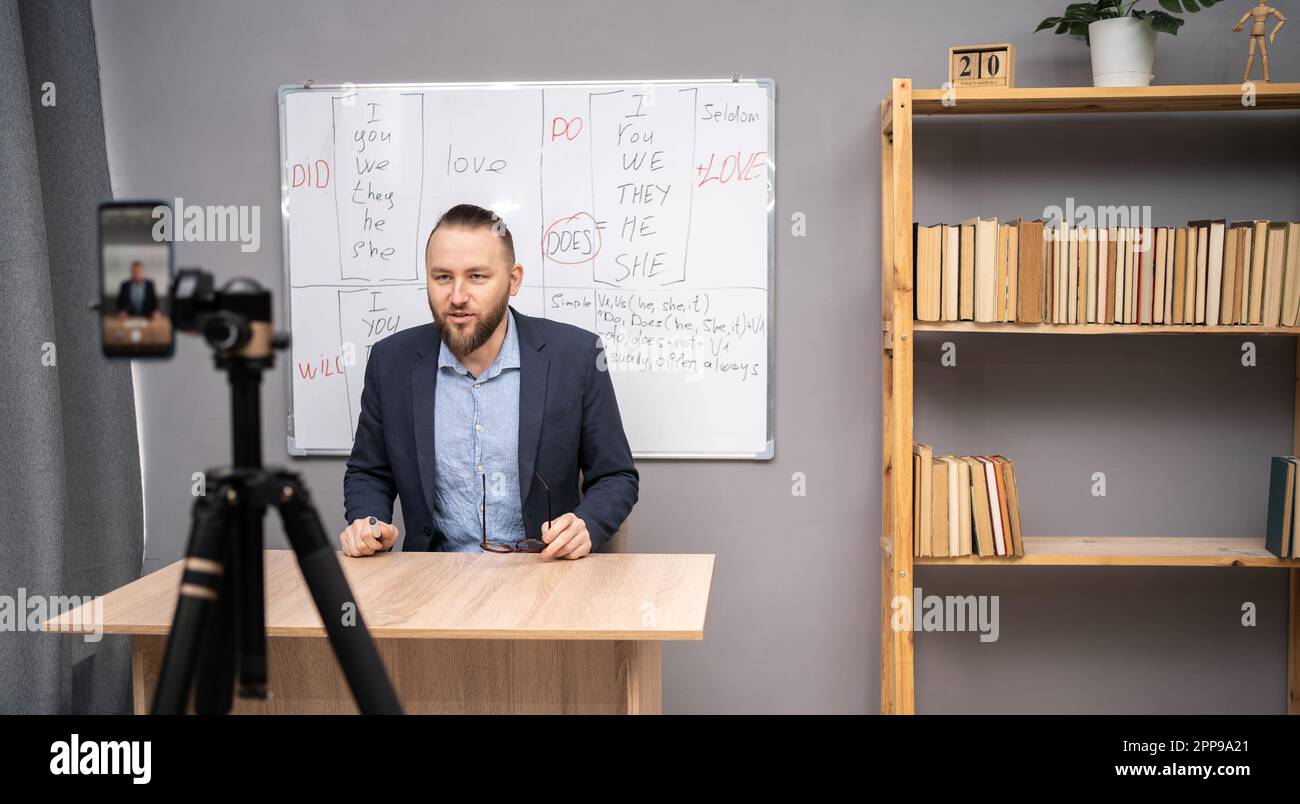 Male English teacher having video conference chat with students and class group, using smartphone. Millennial man talking to webcam, explaining rules Stock Photo