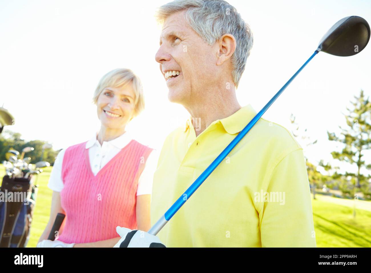 Golfing is their favorite hobby. Attractive elderly couple with their golf clubs over their shoulders. Stock Photo