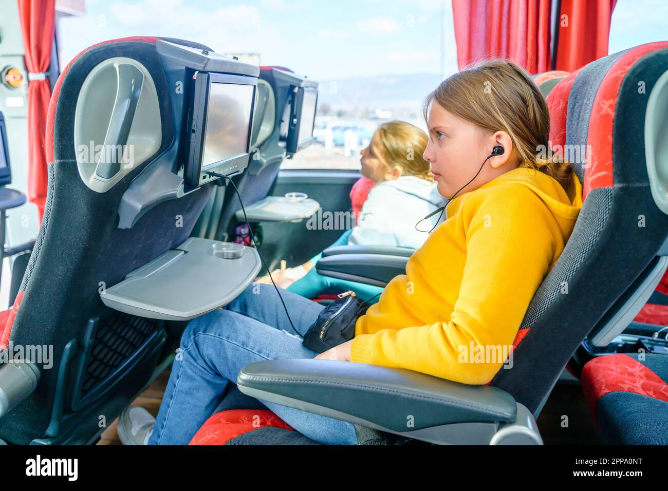Bus road traveling. Girl kid rides on large comfortable sightseeing excursion bus. Watching movie cartoon on screen in chair. Entertainment media syst Stock Photo