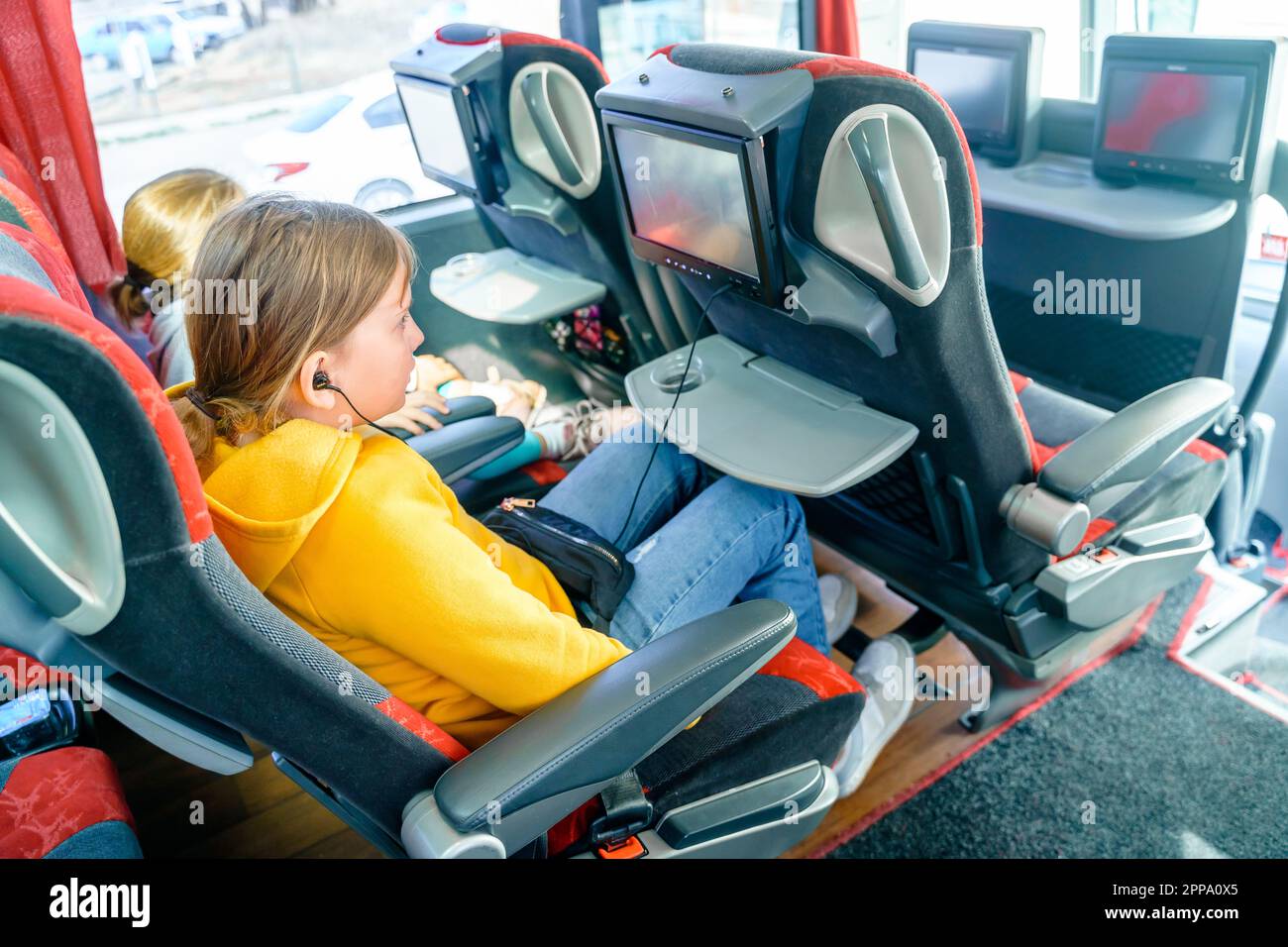 Bus road traveling. Girl kid rides on large comfortable sightseeing excursion bus. Watching movie cartoon on screen in chair. Entertainment media syst Stock Photo