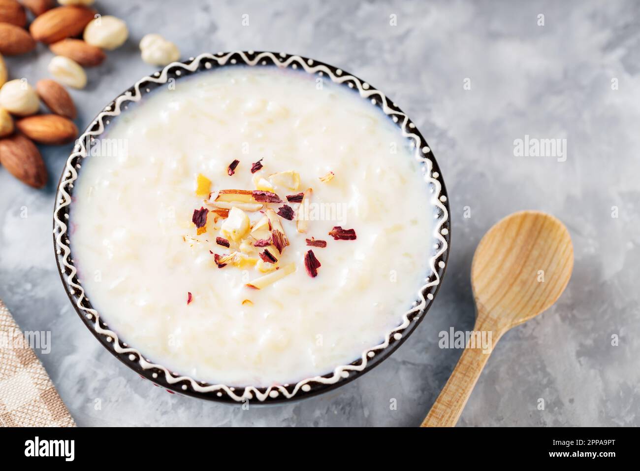 Indian kheer rice pudding with nuts on concrete. Bowl with rice pudding and a wooden spoon on a gray background. Top view Stock Photo