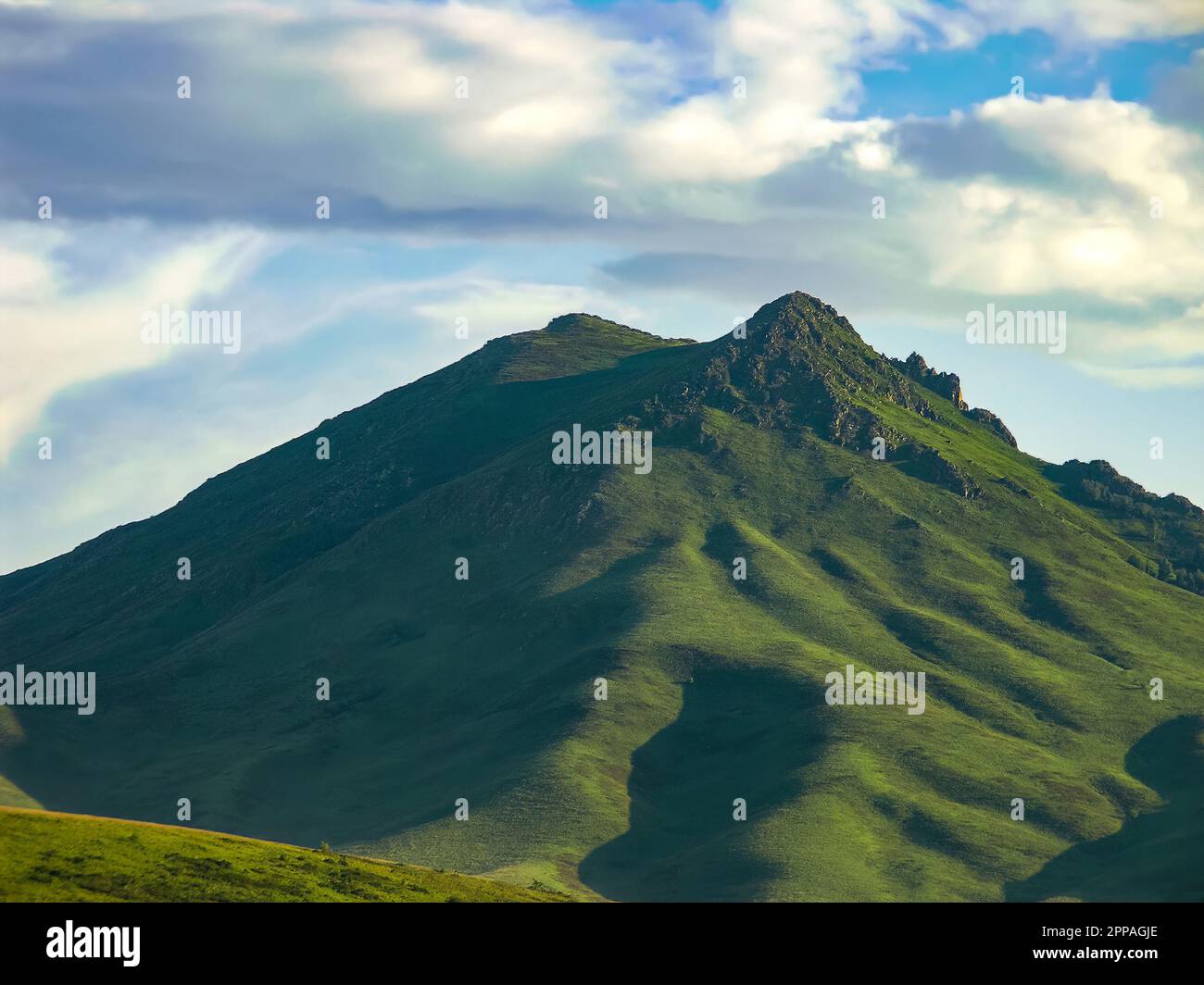 Double top mountain with green slopes against a cloudy backdrop on a summer day. Eagle Mountain, East Kazakhstan, Altai Mountains Region. Stock Photo