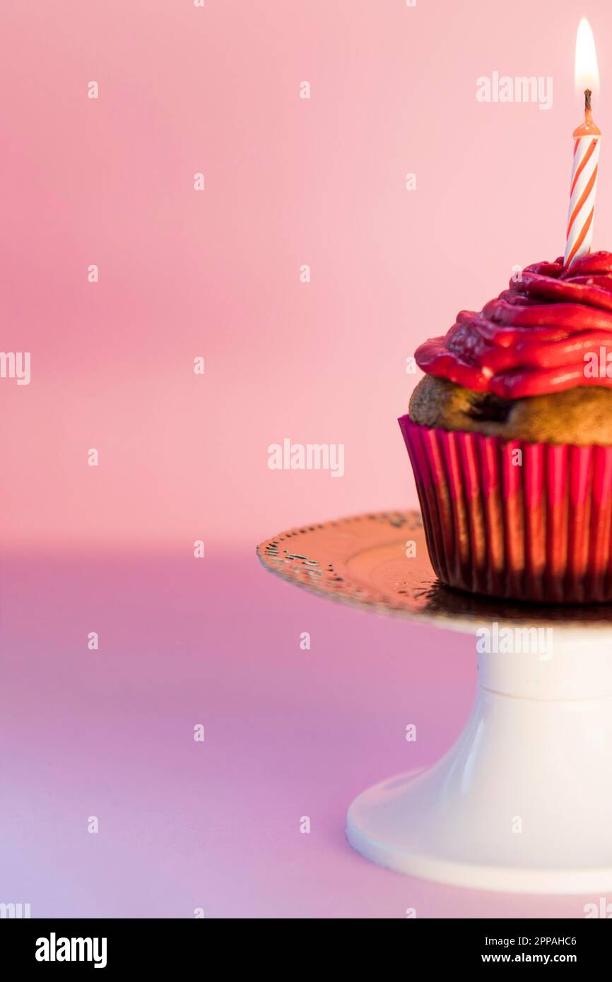 Close up lighted candle cupcake cakestand against pink background Stock