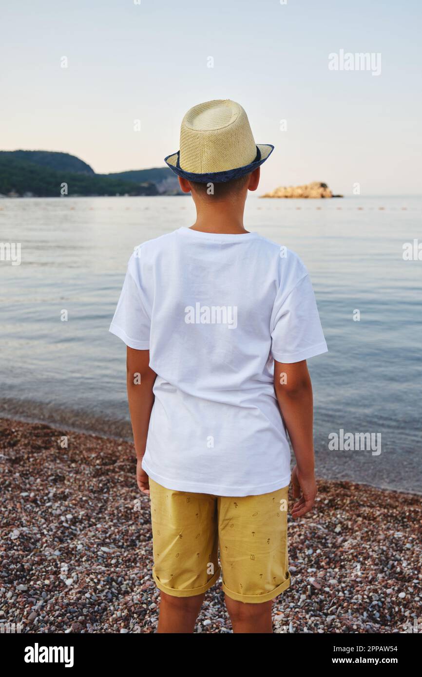 Teenage boy in a straw hat and a white t-shirt looks into the sea