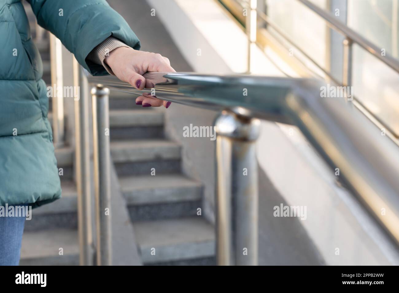 woman holding on to the railing going down the stairs. hand holding the handrail. woman in transit Stock Photo