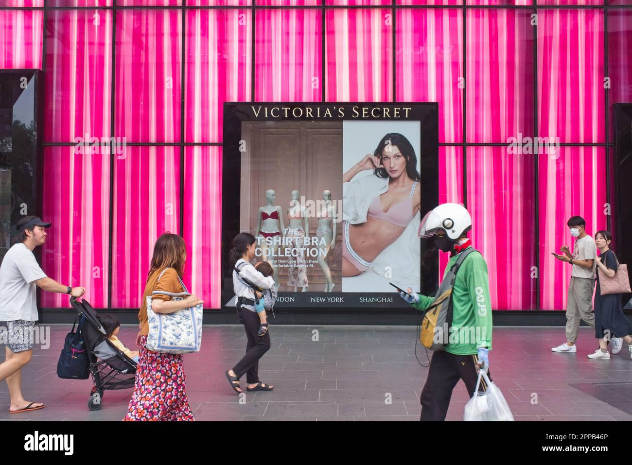 Shoppers and a Grab delivery man pass a pink-themed Victoria's Secret outlet in Orchard Road, Singapore, the city's state's famed shopping street Stock Photo
