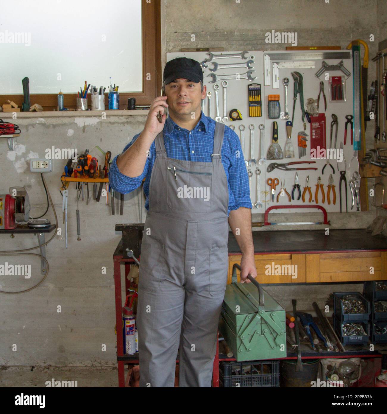 Image of a handyman in his workshop talking on the phone and holding a toolbox. Answering a call for work. Stock Photo