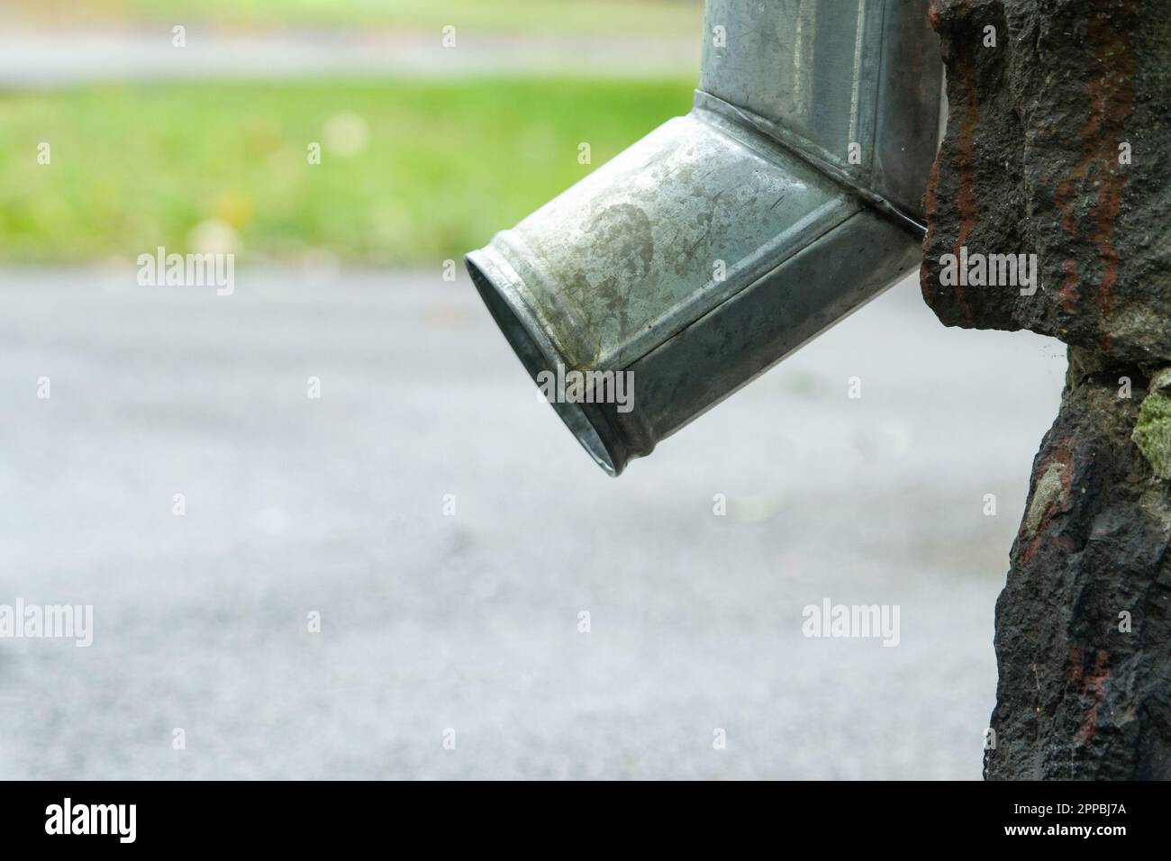 Bottom of downspout at the background of sidewalk and green grass Stock