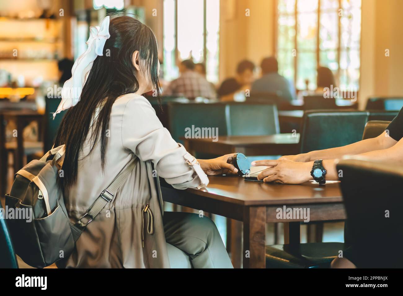 Back view of Asian woman with backpack holding wireless queue caller machine in hand to wait food in restaurant. Alarm signal warning pager in self se Stock Photo