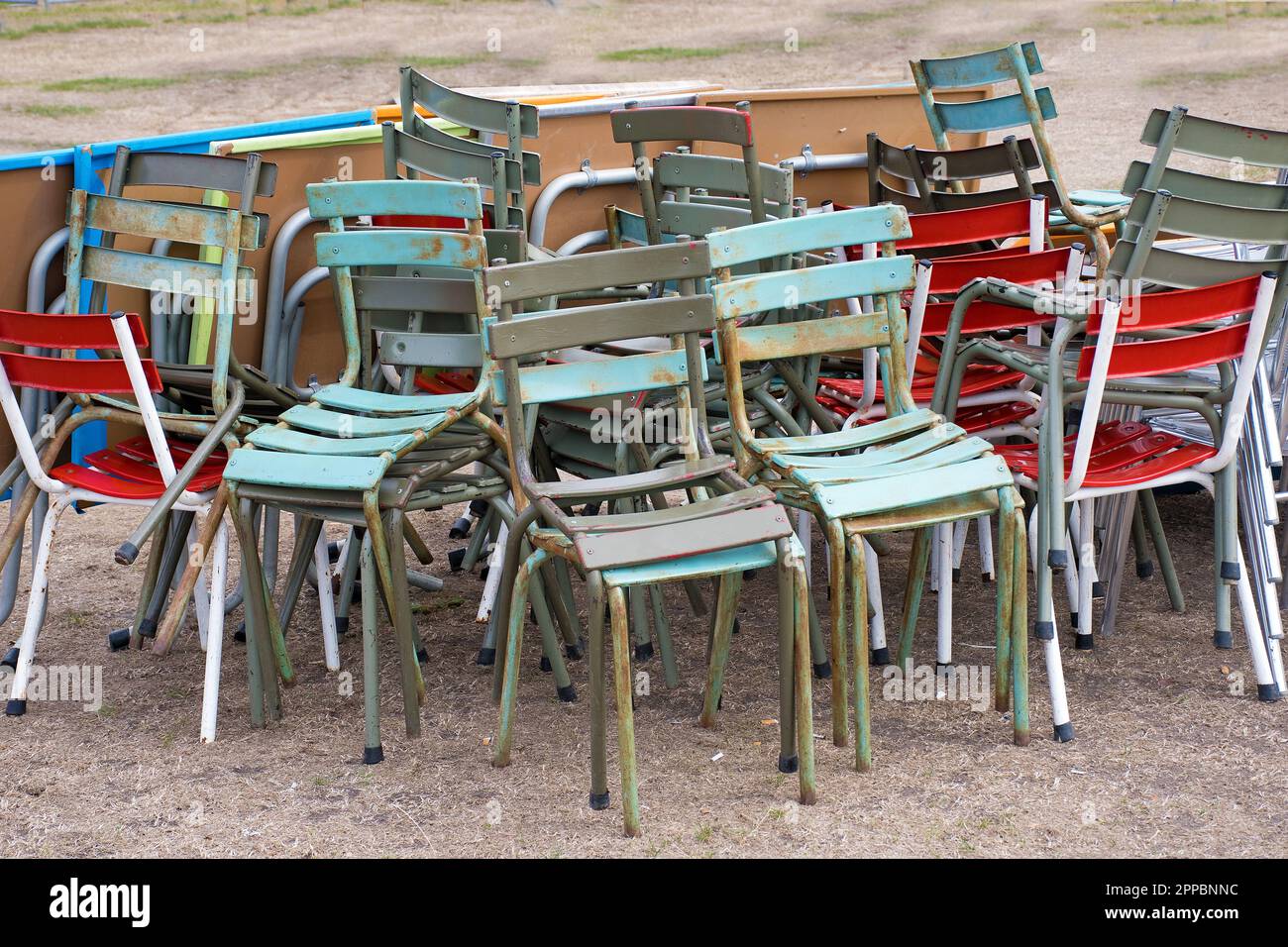 Colourful, old, shabby chairs stacked at the end of the season Stock Photo