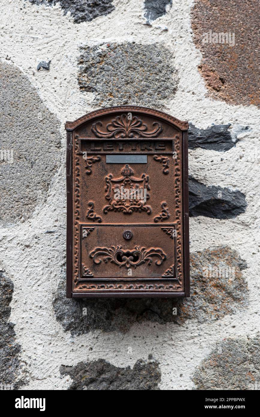Old rust coloured metal letter box against a stone wall, with the word