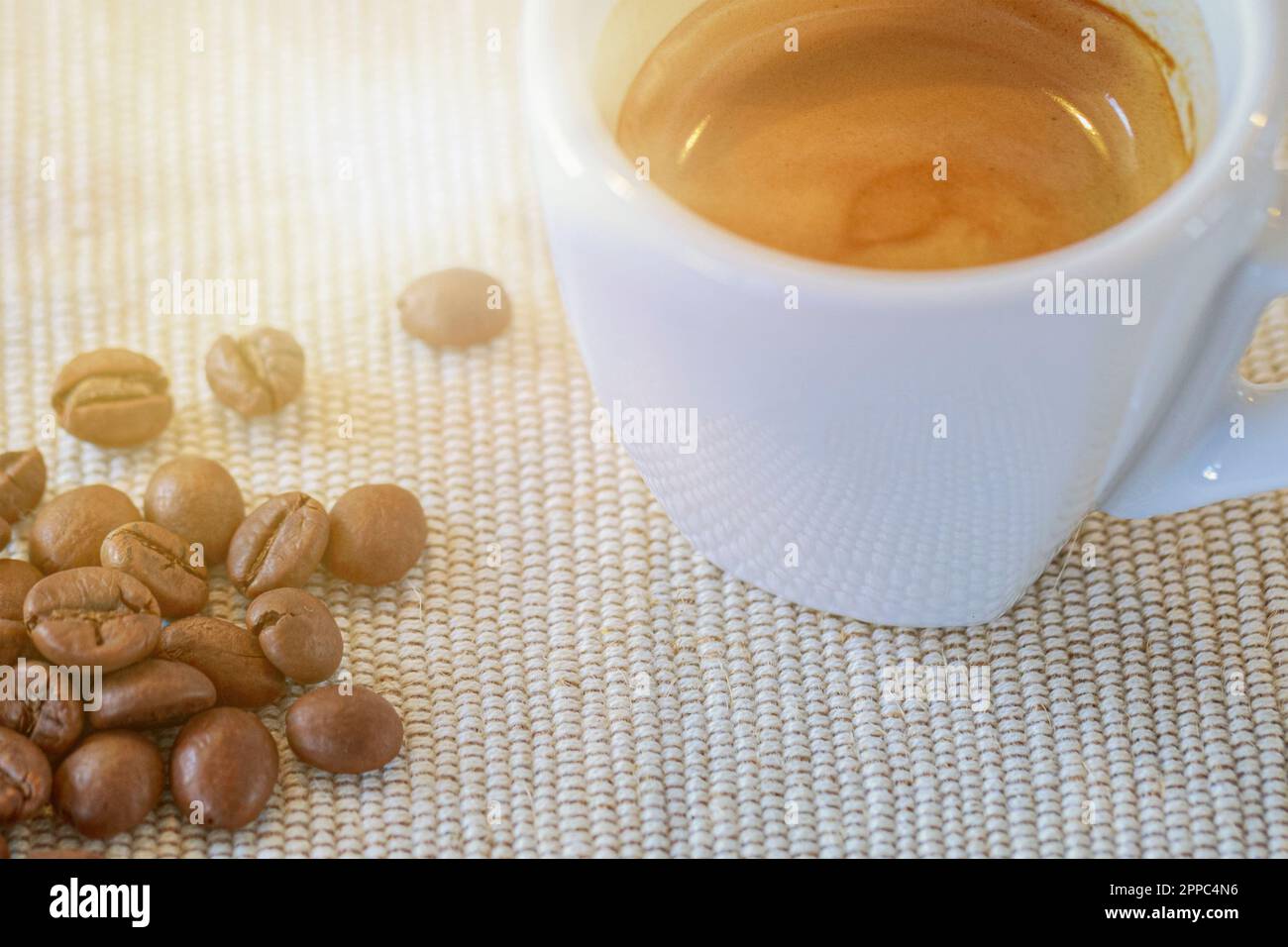 eine gefüllte Espresso Tasse steht neben Kaffeebohnen auf einem Tisch Stock Photo