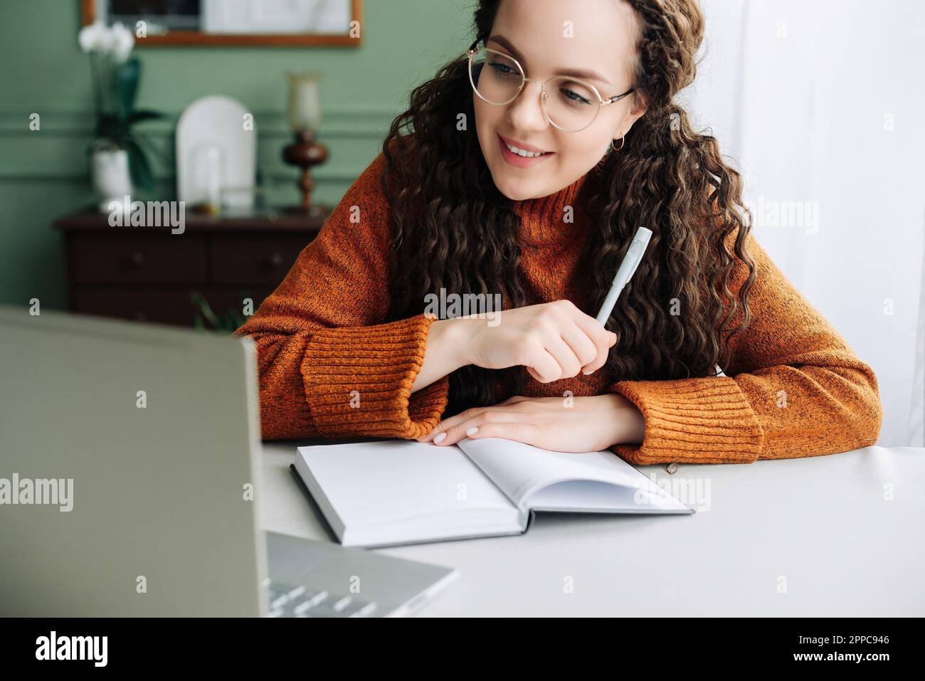 Young smiling pretty woman student using laptop elearning or remote working at home office using laptop computer watching webinar, learning web course Stock Photo