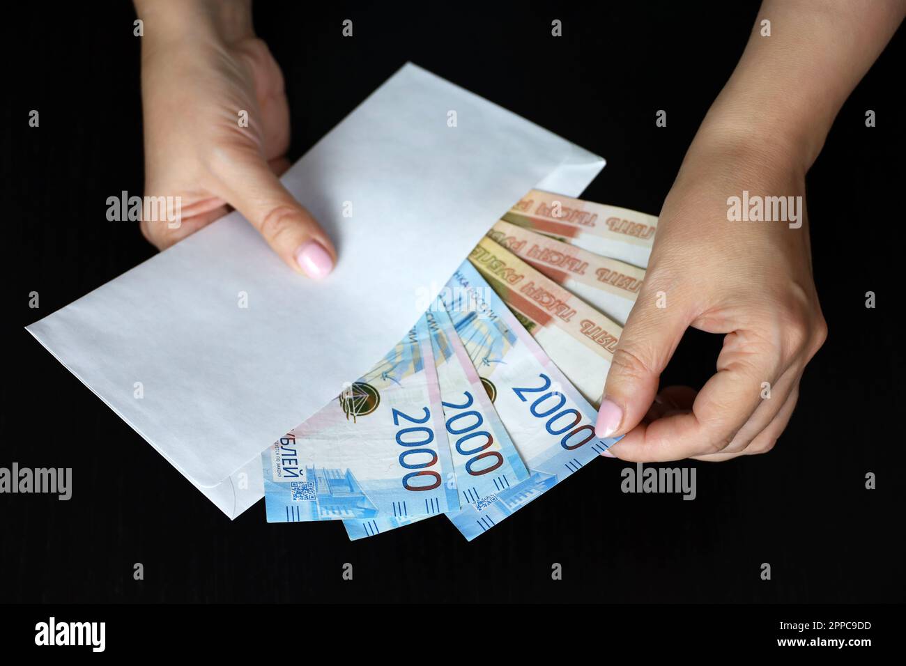 Envelope with russian rubles in female hands on black background. Wages in Russia, bonus or bribe concept Stock Photo