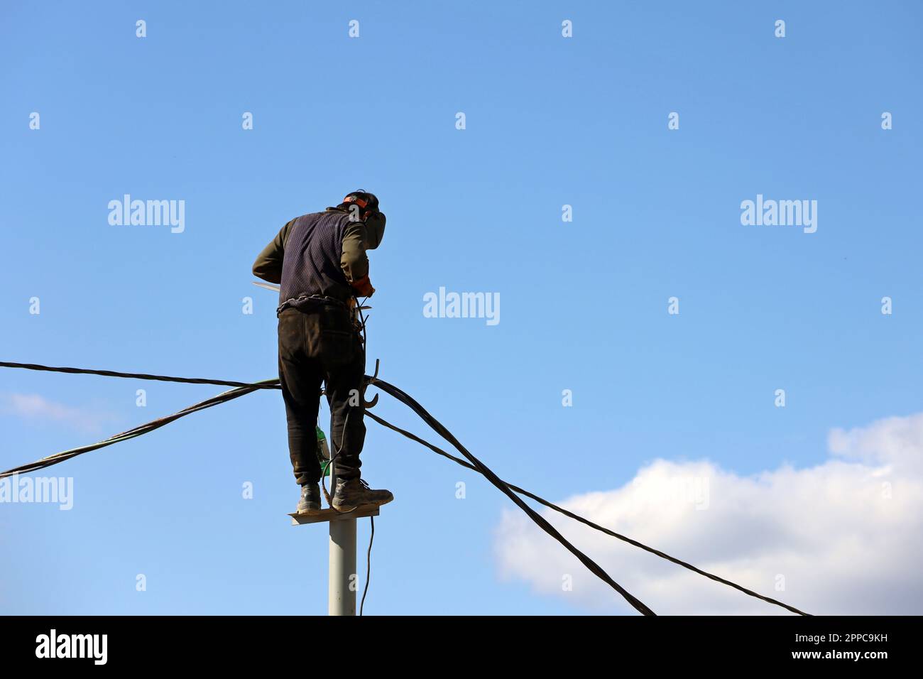 Electrician repairs the electrical wires on a street pole. Worker against the blue sky, concept of street lighting repair, power outages Stock Photo